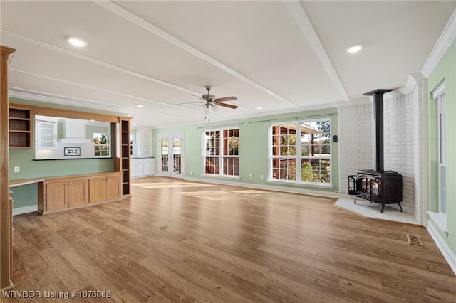 unfurnished living room featuring ceiling fan, a wood stove, ornamental molding, and light hardwood / wood-style flooring