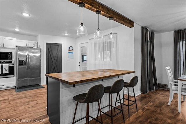 kitchen with wood counters, appliances with stainless steel finishes, white cabinetry, hanging light fixtures, and a breakfast bar area