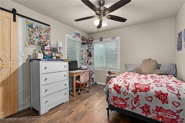 bedroom featuring hardwood / wood-style flooring, ceiling fan, a barn door, and a textured ceiling