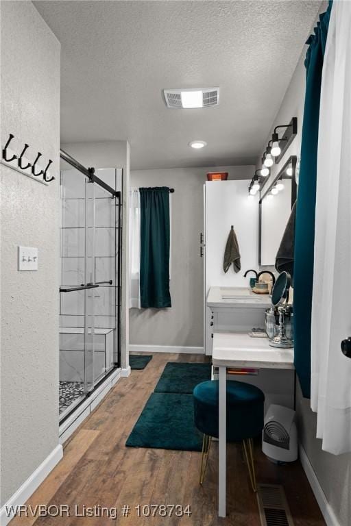 bathroom with hardwood / wood-style floors, sink, an enclosed shower, and a textured ceiling