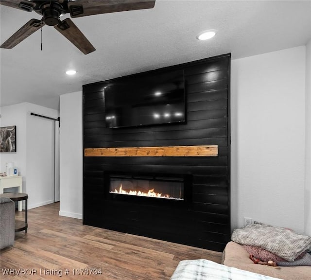 living room with a fireplace, hardwood / wood-style floors, ceiling fan, and a barn door