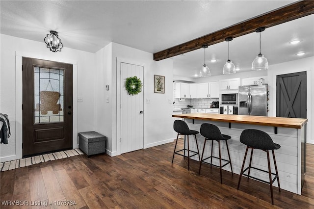 kitchen with appliances with stainless steel finishes, butcher block counters, decorative light fixtures, white cabinetry, and a kitchen bar