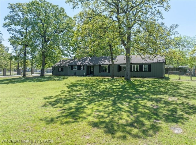 view of front of property with board and batten siding, a front lawn, and fence
