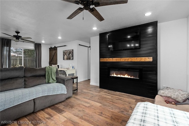 living room featuring ceiling fan, a barn door, a large fireplace, and hardwood / wood-style floors