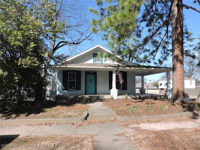 bungalow-style home with covered porch, a carport, and stucco siding