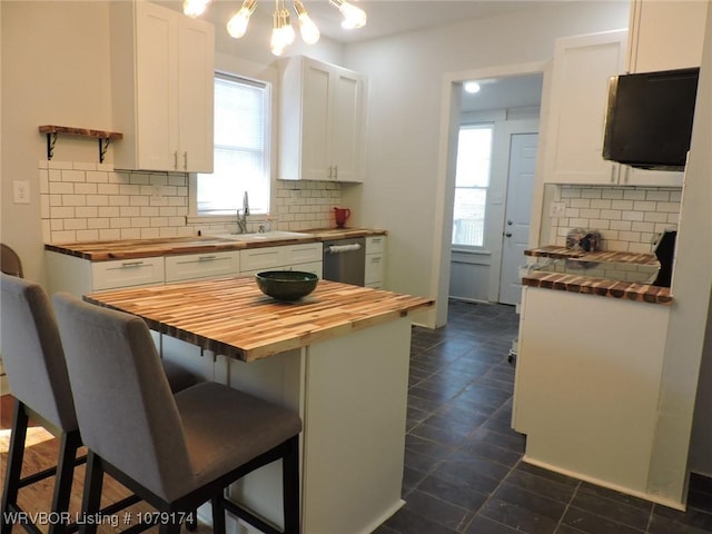 kitchen with a breakfast bar area, white cabinets, wooden counters, stainless steel dishwasher, and tasteful backsplash