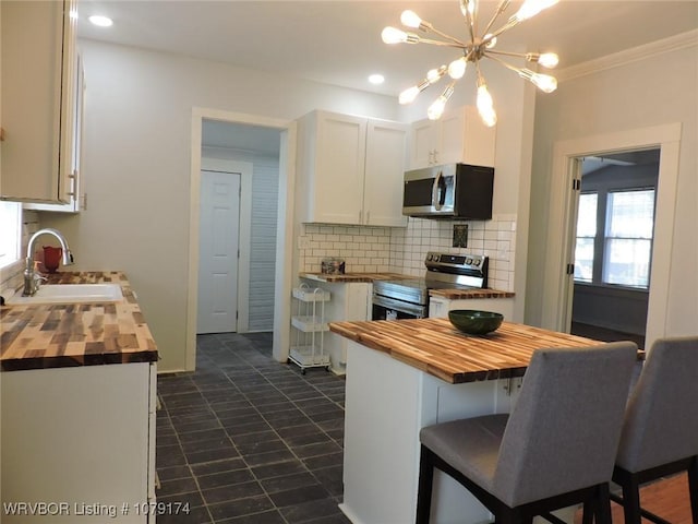 kitchen featuring butcher block countertops, appliances with stainless steel finishes, a sink, white cabinetry, and backsplash