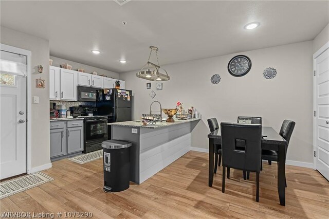 kitchen with kitchen peninsula, black appliances, light hardwood / wood-style floors, white cabinetry, and hanging light fixtures