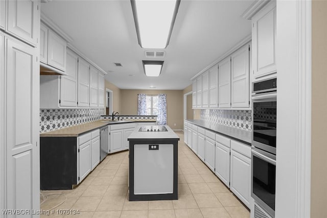 kitchen with a center island, white cabinets, sink, light tile patterned floors, and tasteful backsplash