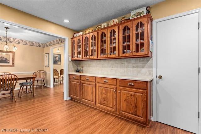 kitchen with tasteful backsplash, light hardwood / wood-style flooring, a textured ceiling, and a notable chandelier