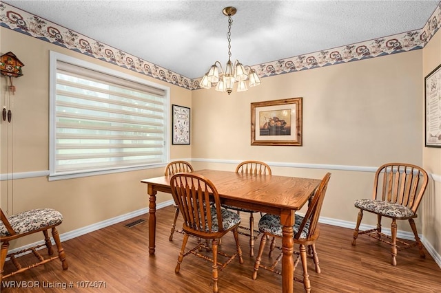 dining area with wood-type flooring, a textured ceiling, and a notable chandelier