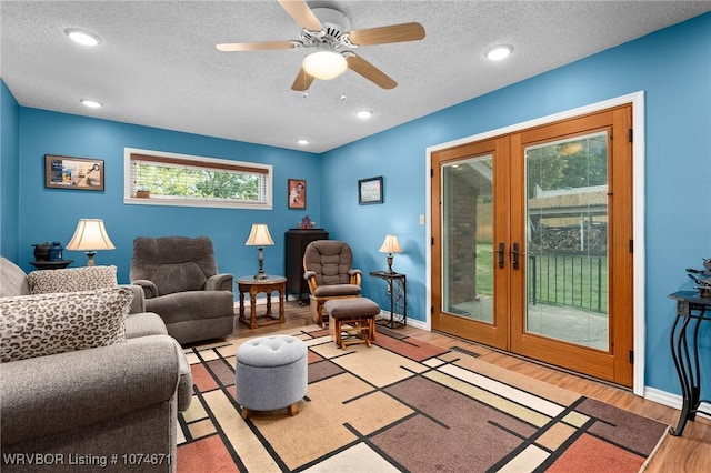 living room featuring ceiling fan, french doors, light hardwood / wood-style floors, and a textured ceiling