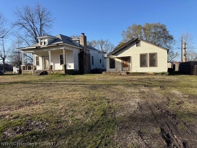 rear view of house featuring a yard, covered porch, and a chimney