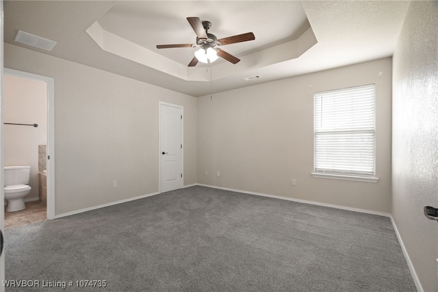 unfurnished bedroom featuring ceiling fan, a raised ceiling, carpet floors, and ensuite bath