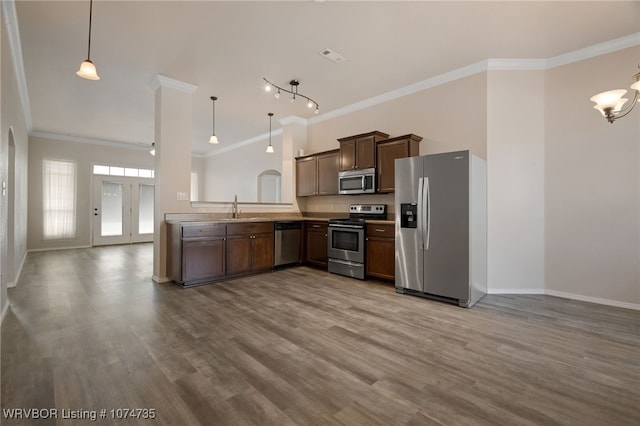 kitchen with kitchen peninsula, appliances with stainless steel finishes, sink, pendant lighting, and light hardwood / wood-style flooring