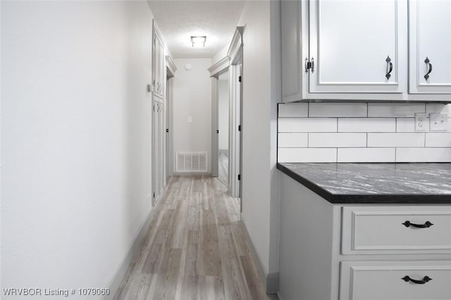 hall with light wood-style flooring, visible vents, and baseboards