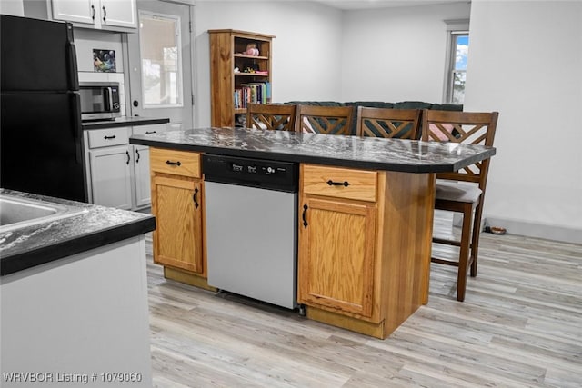 kitchen featuring dark countertops, a kitchen island, a breakfast bar, stainless steel appliances, and light wood-type flooring