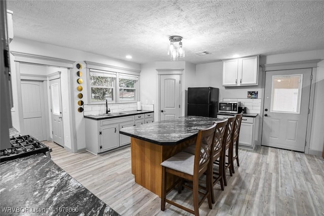 kitchen with a breakfast bar, light wood-style floors, a sink, a kitchen island, and black appliances