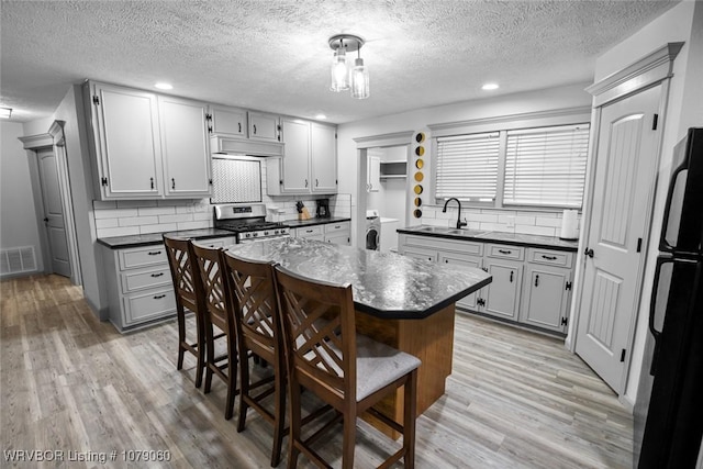 kitchen with under cabinet range hood, a sink, visible vents, stainless steel gas range, and dark countertops