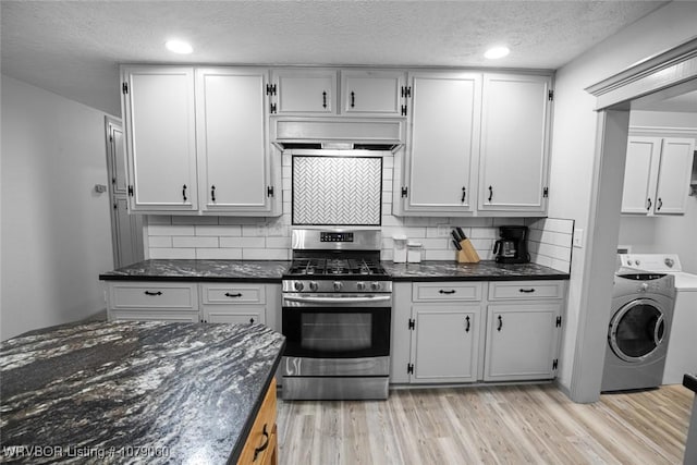 kitchen with light wood finished floors, washer / dryer, dark stone counters, stainless steel gas range oven, and wall chimney exhaust hood