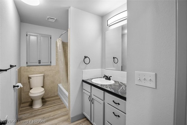 bathroom featuring visible vents, toilet, wood finished floors, shower / bath combo with shower curtain, and vanity