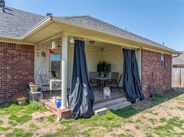 back of property with brick siding, roof with shingles, and fence