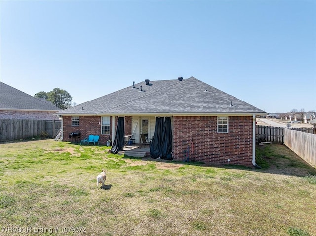 rear view of house featuring a lawn, brick siding, a fenced backyard, and roof with shingles