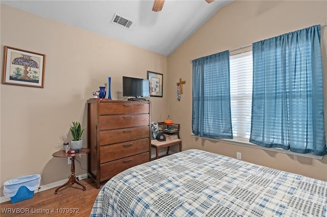 bedroom featuring a ceiling fan, wood finished floors, visible vents, baseboards, and lofted ceiling