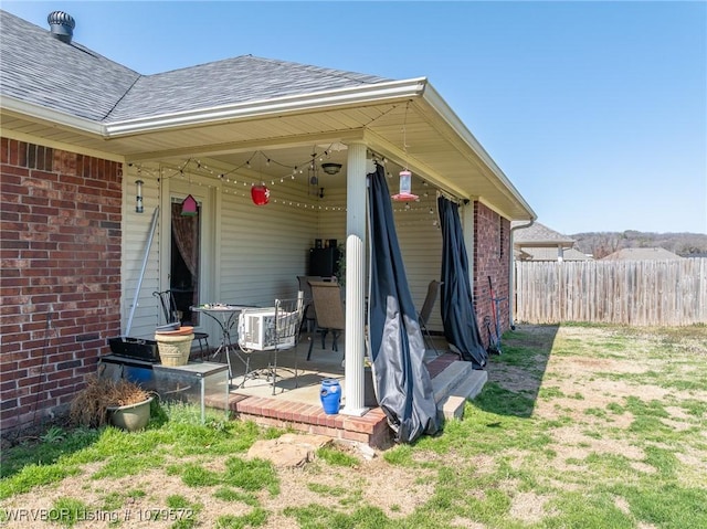 entrance to property with brick siding, roof with shingles, and fence