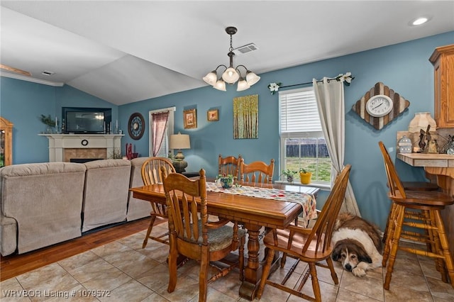 dining space with visible vents, a notable chandelier, a tiled fireplace, and vaulted ceiling