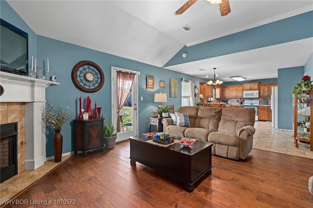 living room with wood finished floors, ceiling fan with notable chandelier, visible vents, and a tile fireplace