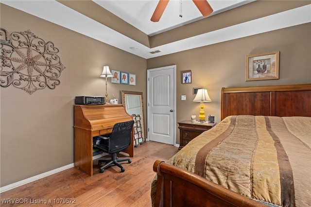 bedroom featuring visible vents, baseboards, a tray ceiling, wood finished floors, and a ceiling fan