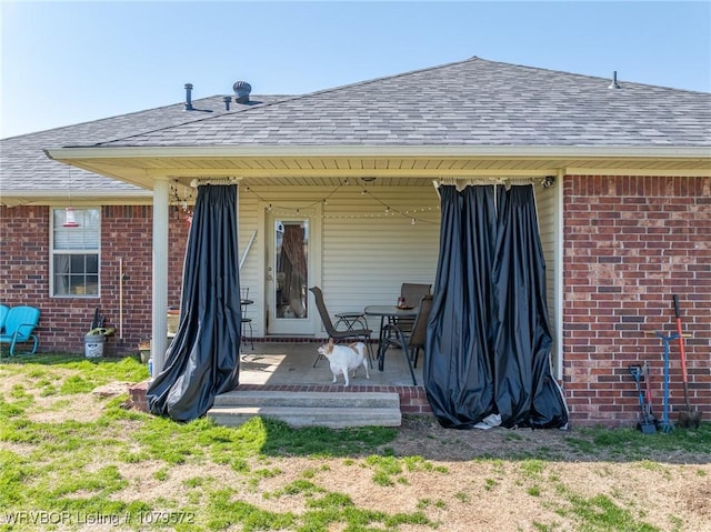 rear view of property featuring brick siding, a patio, and roof with shingles