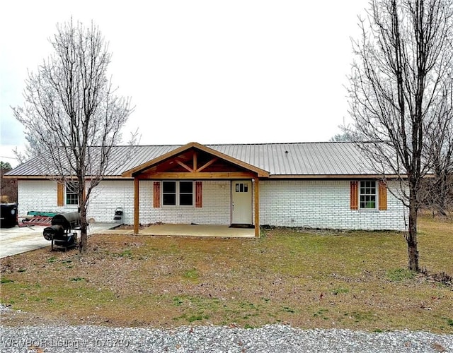 ranch-style home with a front yard, metal roof, brick siding, and a patio