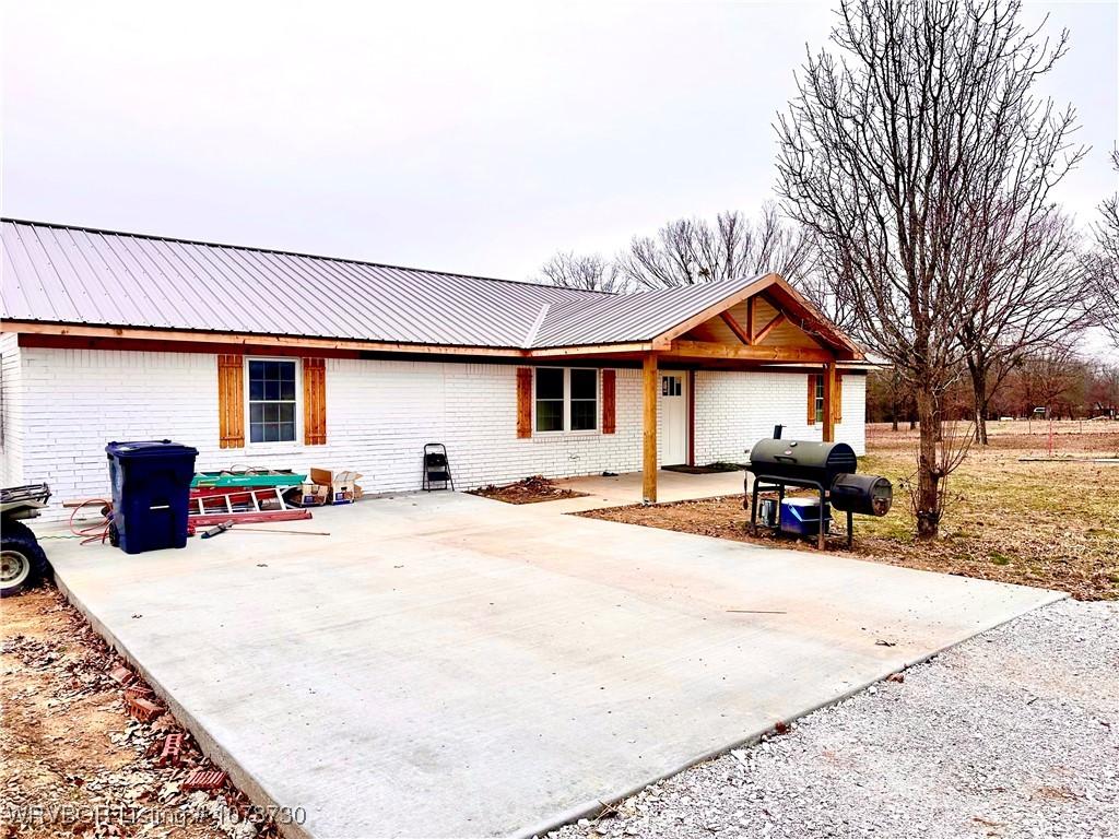 ranch-style house featuring brick siding, metal roof, driveway, and a patio