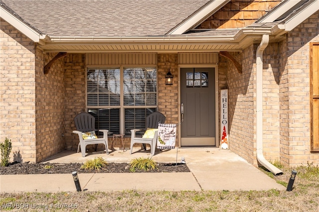 doorway to property featuring brick siding and roof with shingles