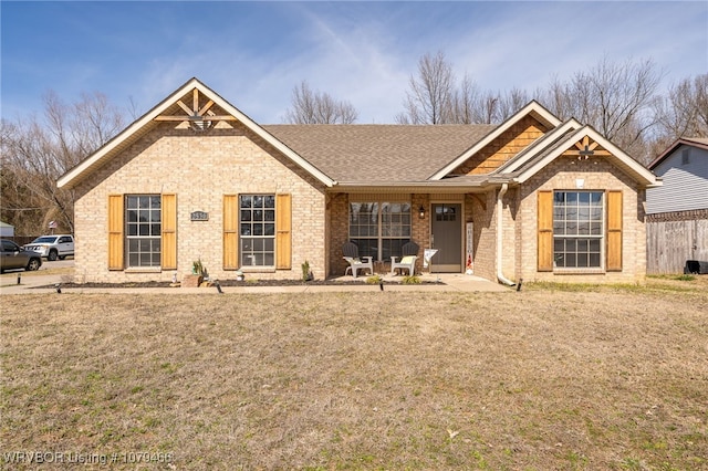 view of front of property with roof with shingles, a front lawn, and brick siding