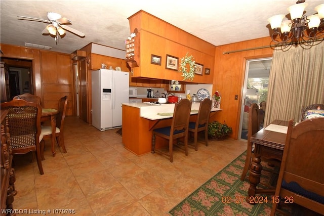 kitchen featuring wood walls, white appliances, ceiling fan with notable chandelier, a kitchen bar, and kitchen peninsula