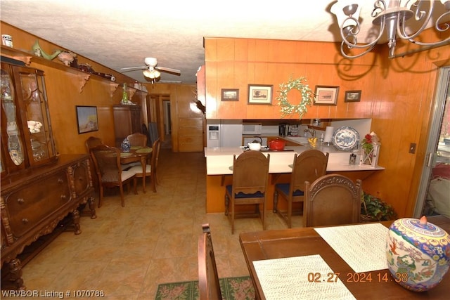 dining room featuring wooden walls, ceiling fan with notable chandelier, and a textured ceiling