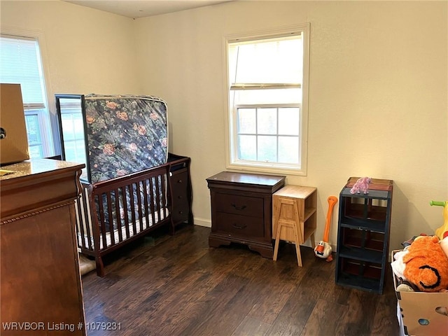 bedroom featuring a nursery area and dark wood finished floors