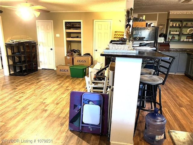 kitchen with a textured ceiling, a breakfast bar area, dark countertops, and wood finished floors