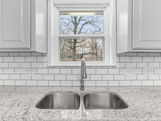 details with light stone counters, sink, tasteful backsplash, and white cabinets