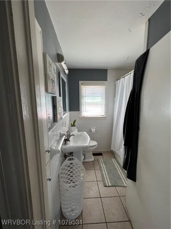 bathroom with tile patterned floors, a shower with curtain, toilet, a sink, and tile walls