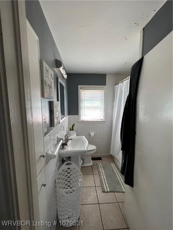 full bath with toilet, wainscoting, a shower with curtain, tile patterned floors, and tile walls