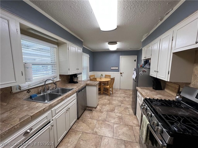 kitchen with a wainscoted wall, ornamental molding, appliances with stainless steel finishes, white cabinets, and a sink