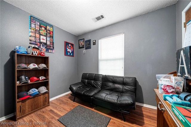 living room with a textured ceiling, wood finished floors, visible vents, and baseboards