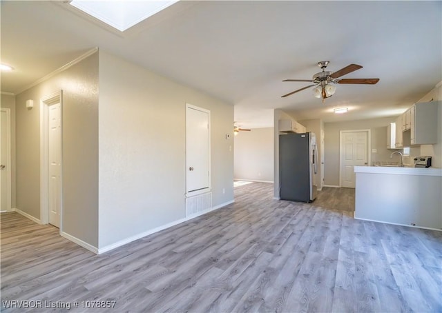 kitchen with sink, stainless steel fridge, ceiling fan, a skylight, and light wood-type flooring