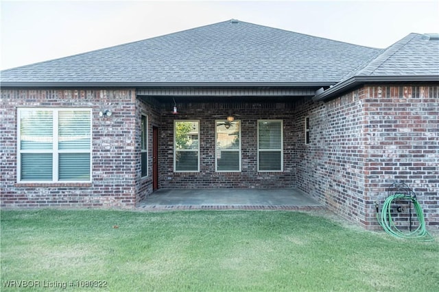 rear view of house featuring a lawn, brick siding, a patio, and a shingled roof