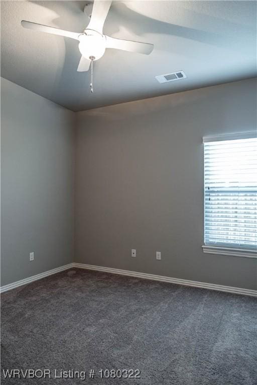 spare room featuring dark colored carpet, visible vents, baseboards, and ceiling fan