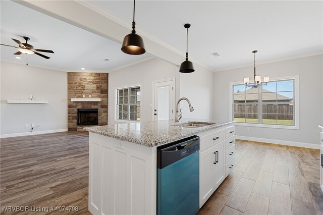 kitchen with a kitchen island with sink, sink, stainless steel dishwasher, light stone counters, and white cabinetry